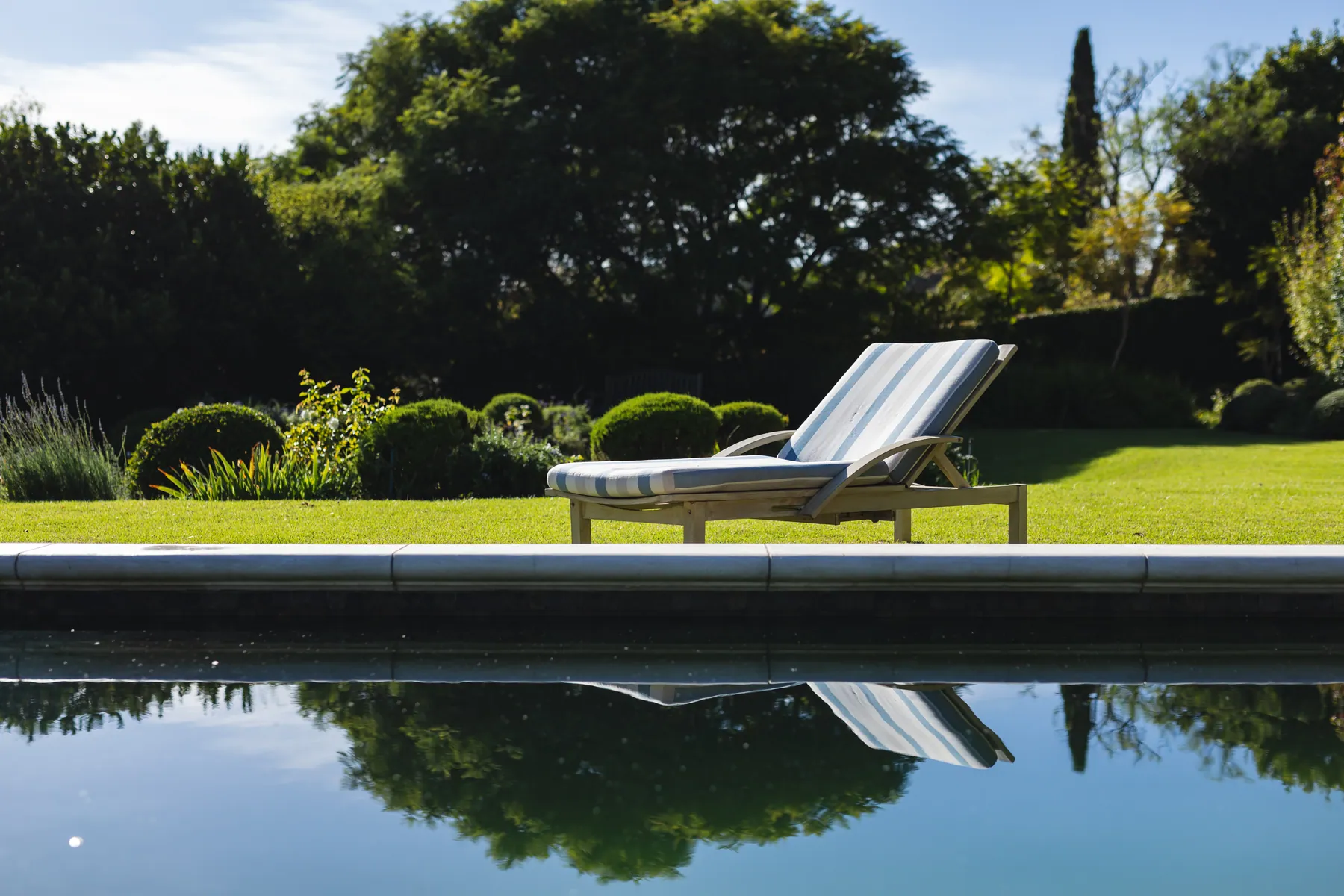 Naturpool mit Liege und Spiegelung im klaren Wasser
